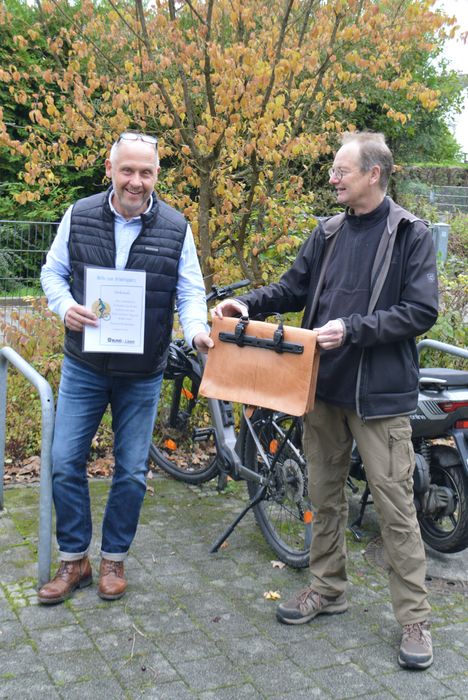 Michael Heitkämper (links) erhält von Stephan Culemann die zur Fahrradtasche umgerüstete Lederschultasche mitsamt Urkunde als Auszeichnung.